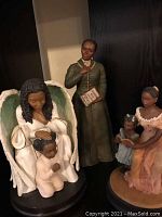 Photo showing three resin inspirational figurines: an angel with child, a standing man with a book, and a woman with two children.