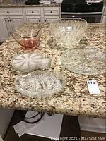 Overall image of glass serving pieces including bowls, trays, and luncheon plates on granite countertop.