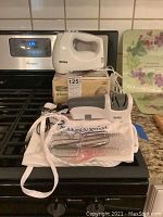 Photo showing the Kenmore hand mixer on its original box, the Smiths electric sharpener, hand mixer beaters and a white apron laid out on a kitchen stove.