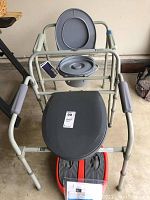 Lightly used commode chair with gray padded seat, lid opened showing commode bucket.