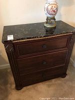 Full view of wooden nightstand showing three drawers, metal knobs, and faux marble top surface with a decorative item on top.