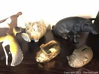 Four piggy banks of various materials on a shelf: brass, cast iron (hippo-shaped), and pottery. Two balancing plastic birds in yellow and brown also visible.