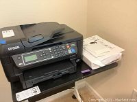 Epson WorkForce WF-2750 printer with paper and software package beside it on a small table.