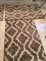 Three large taupe and cream patterned bathroom rugs arranged on a floor showing size and pattern.