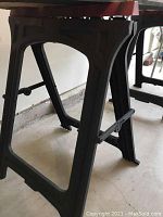 Side view of one black plastic folding sawhorse showing sturdy legs and locking arm