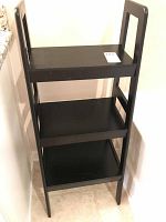 Full view of black wooden shelf with three shelves on tile floor, show structure and condition