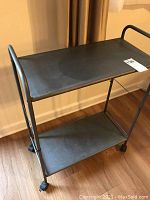 Front-side angled view of shelf showing top and bottom shelves, metal rounded side bars, and caster wheels.