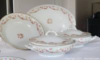 Porcelain set including two covered bowls, one open bowl, and oval platter with bridal wreath pink rose swag pattern and gold zigzag edging.