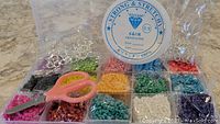 Overall kit of 15 colors of glass seed beads, spool of strong stretchy cording, and pink handled scissors.