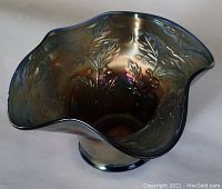 Top view showing the wavy scalloped rim and raised holly leaf and berry pattern with iridescent cobalt blue finish.