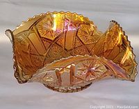 Side angle view of marigold carnival glass dish showing ruffled edges, star and file relief pattern, and iridescent finish.