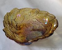 Front angled view of the marigold carnival glass dish showing detailed leaf and berry embossed pattern and iridescent finish.