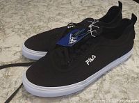 Pair of black Fila sneakers with white soles and black laces, tags still attached indicating they are unused.