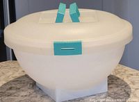 Full view of large oval plastic salad bowl with white lid and turquoise handle and latches on countertop.