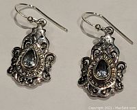 Front view of the pair of ornate sterling silver earrings with blue topaz stones at center, hook style.