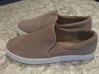 Side angle view of taupe suede slip-on loafers with white sole on granite surface.