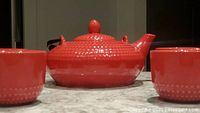 Front view of red ceramic teapot on flat surface showing body and spout