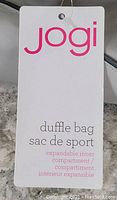 Close-up of Jogi duffle bag tag showing brand name and expandable inner compartment detail