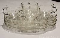 Four clear glass luncheon plates stacked with four matching cups arranged on top, showing the clear textured swirl pattern on plates and twisted glass handles on cups.