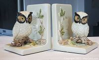 Pair of vintage ceramic owl bookends, cream colored with brown and green leafy branch design, both shown side by side