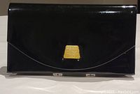 Front view of black patent leather look clutch showing gold clasp