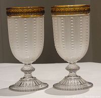 Front view of two vintage frosted pressed glass goblets with amber colored rims placed side by side, showing full height and decorative details on rims and bases.