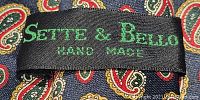 Close-up image of black label sewn inside tie reading 'Sette & Bello HAND MADE' embroidered in green thread.
