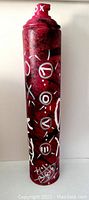Front view of the tall spray can painted dark red and black with white graphic symbols on the surface.