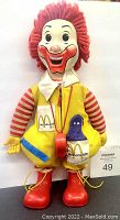 Full view of 20-inch 1978 Hasbro Ronald McDonald doll in yellow vest, striped sleeves, red shoes, yarn hair, and whistle around neck, holding Grimace toy in vest pocket.