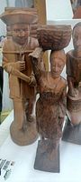 Close-up photo of the three carved wooden statues showing the Woodsman carrying wood, and the Haitian Woman carrying a basket.