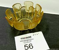 Yellow translucent glass dish with scalloped edge and vertical panel texture seen from above on a black surface.