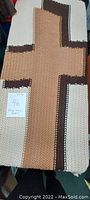 Full view of large crocheted blanket featuring a central cross pattern in beige and brown colors.