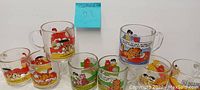 Eight clear glass mugs from vintage Garfield comic series, showing various character prints and labels.