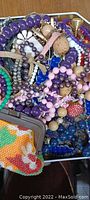 Close-up photo showing assorted colorful beaded necklaces, bracelets, and a large collectible tin edge