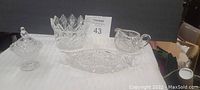 Photo showing all four crystal dishes on a table including the bowl, canoe, creamer, and covered trinket dish with bird on top.