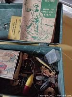 Open tackle box showing various fishing lures, fishing hooks box, fishing line, and 'How to Catch More Fish' guide booklet