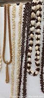 Close view of multiple Hawaiian lei necklaces showing various materials and designs including braided seed beads, small shells, and large white shells.
