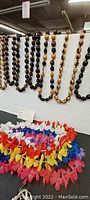 Kukui nut leis hanging with polished nuts in assorted natural shades and silk flower leis laid out in bright colors