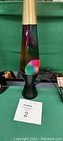 Front view of the lava lamp showing the purple liquid and multicolored wax inside the clear glass container with black base and gold top.