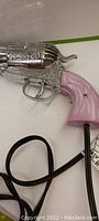Close-up side view of the blow dryer shaped like a Colt revolver with pink handle on white surface