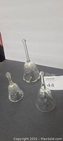 Three clear crystal collectible bells with detailed cut patterns placed on a black surface against a white background.