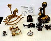 Group photo of all items in the lot showing brass rocking horse candle holder, miniature horse and carriage, antique style phone, opera binoculars, miniature cash register, two fans, and pocket watch.