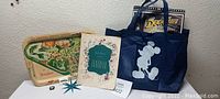 Photo showing the collectible tin tray with Disneyland map, Fantasia program, Mickey Mouse watch face, and a blue shopping bag with DuckTales poster partially visible.
