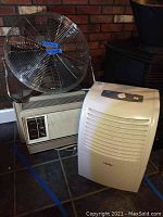 First photo showing the three appliances grouped: the standing fan, the Haier dehumidifier, and the GE window air conditioner below the fan.