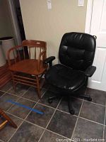 Black office chair and wooden chair side by side on tiled floor.