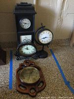 Four clocks including Twos Company wall clock with key cabinet and three assorted tabletop clocks on countertop.