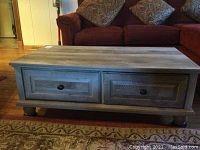 Front view of coffee table showing gray wood grain finish, two drawers, and bun feet