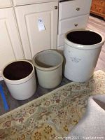 Three ceramic crocks of varying sizes arranged on a rug with kitchen cabinets in the background