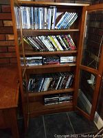 Wooden cabinet shelf filled with multiple DVD movie cases, showing a large collection stored neatly.