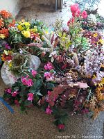 Wide view of numerous faux flower arrangements in various pots and baskets, displayed indoors on floor showing condition and variety